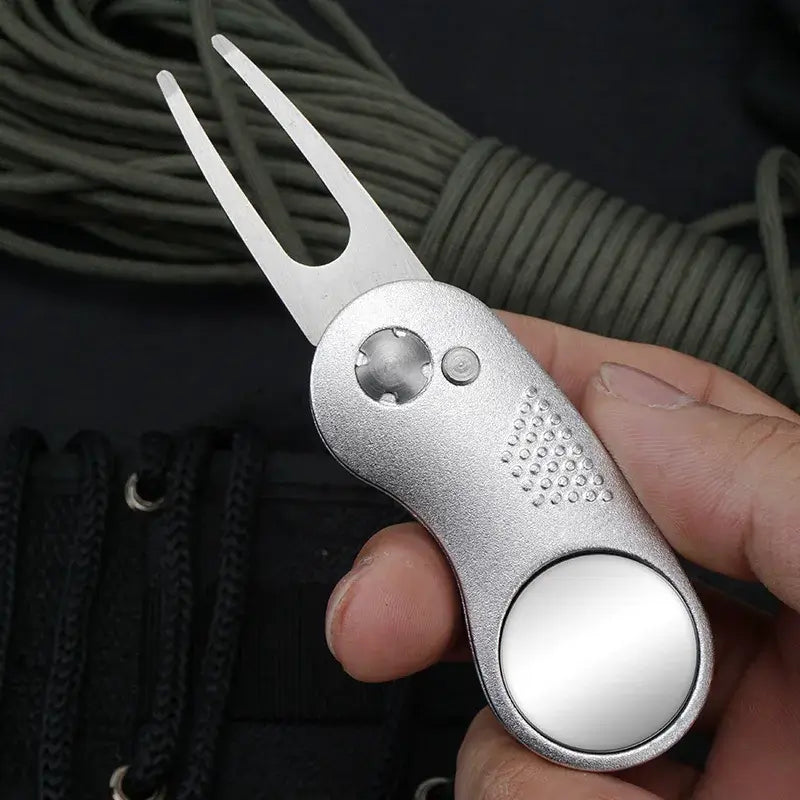 Metal Foldable Golf Divot Repair Tool held in hand with reflective surface and ergonomic design.