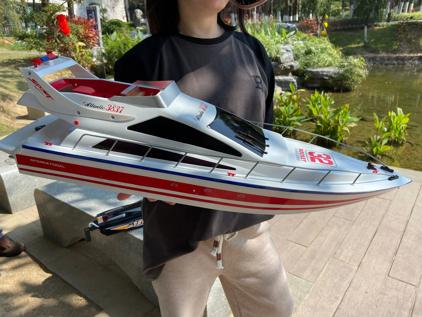 Person holding a Super large remote control yacht, displaying its sleek design at an outdoor lakeside location.