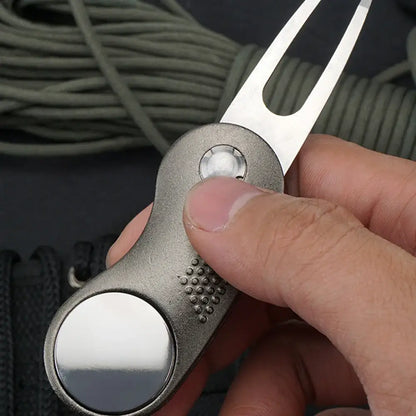 Close-up of a hand holding a Metal Foldable Golf Divot Repair Tool with a shiny forked end.