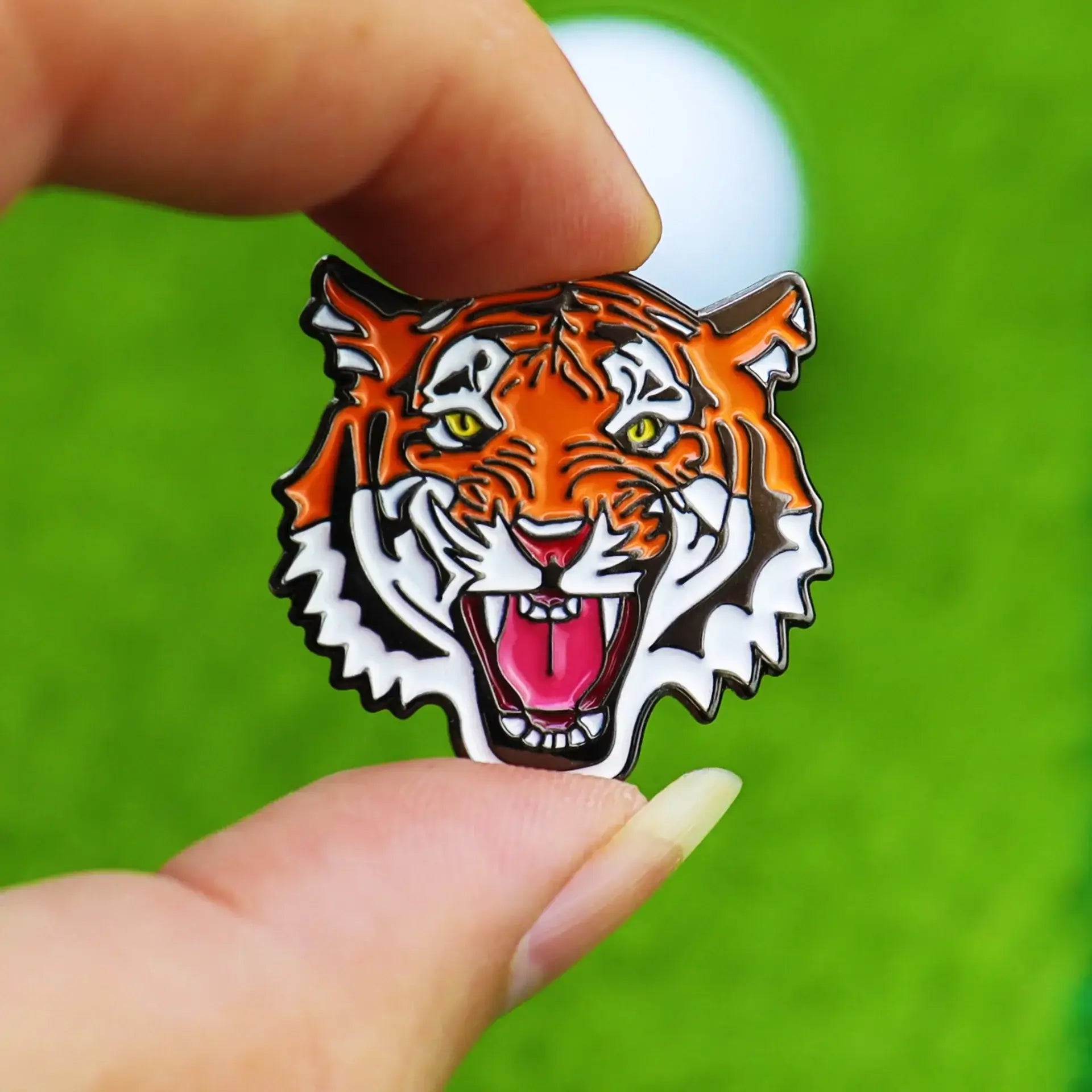 Tiger head golf ball marker hat clip held in hand, vibrant colors on green grass background.