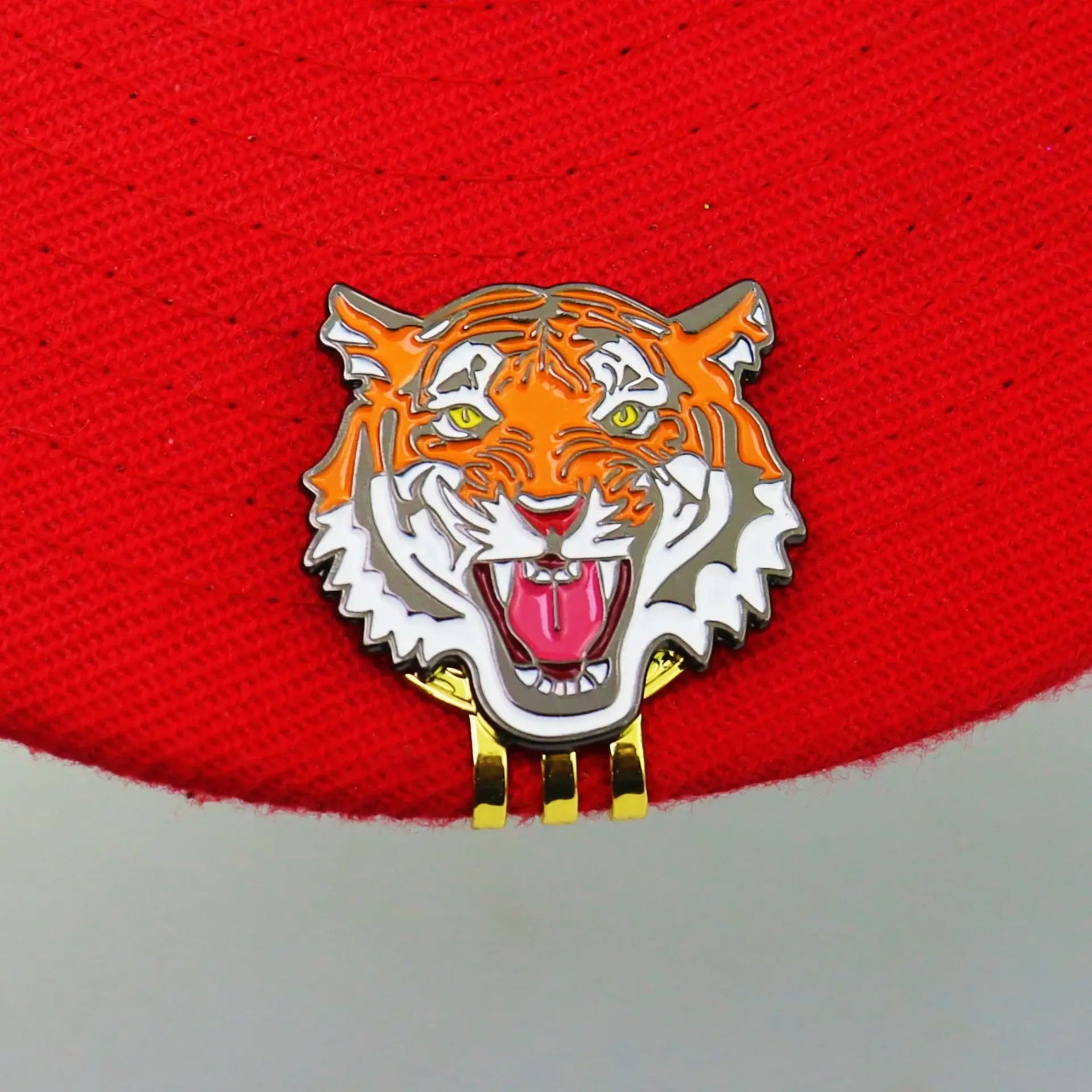 vibrant tiger head design golf ball marker hat clip attached to a red hat, perfect for golf enthusiasts