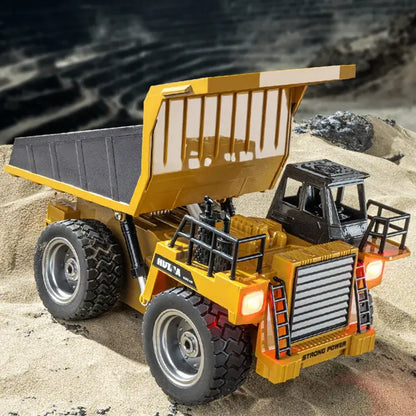 Huina 533D Alloy Remote Control Dump Truck in a sandy environment with its dump bed raised.
